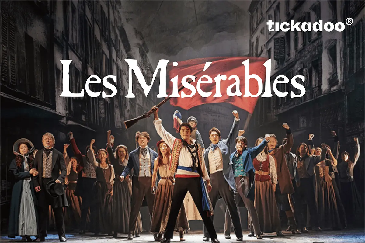 Giftcard featuring a dramatic scene from Les Misérables with people in 19th-century French attire raising fists, red flag, dark city backdrop, tickadoo logo in the top right corner.